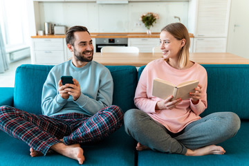Obraz premium Portrait of young joyful couple using cellphone and reading book