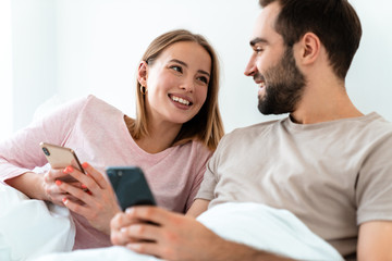 Portrait of beautiful joyful couple smiling and using smartphones