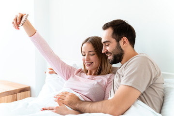 Fototapeta premium Portrait of joyful couple hugging and taking selfie photo on smartphone