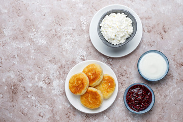 Cottage cheese pancakes.Russian syrniki or sirniki, cottage cheese fritters or pancakes with a bowl of fresh homemade cottage cheese on light background
