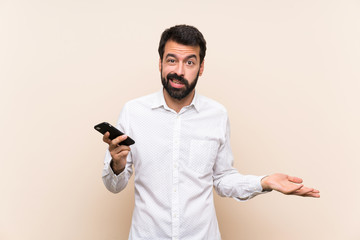 Young man with beard holding a mobile unhappy for not understand something