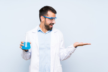 Young scientific holding laboratory flask over isolated background holding copyspace with two hands
