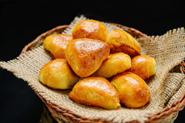 Delicious rustic pastries filled with meat and vegetables in a basket on black background.