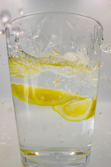 lemon dropping into a glass of water with bubbles and a splash isolated on a white background