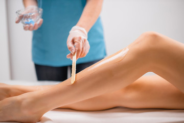 Obraz na płótnie Canvas side view on professional beautician applying moisturizer on female legs before laser epilation procedure. slender woman lie on bed, she want soft, hairless and smooth skin