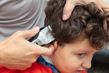 Naklejka premium The hairdresser cuts the hair of a boy with a machine