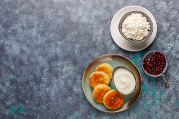 Cottage cheese pancakes with raspberry jam.Russian syrniki or sirniki, cottage cheese fritters or pancakes with a bowl of fresh homemade cottage cheese on dark grey background
