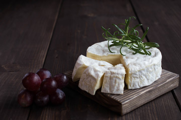Camembert cheese, red grapes ,fresh rasmarin on a wooden stand on a dark wood background
