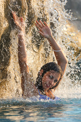 A girl bathes in the spray of a waterfall