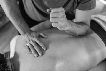 A young sports massage therapist applying pressure with the elbow. Therapeutic body massage treatment. Black and white toned image