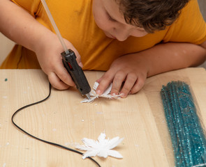 A boy glues snowflakes on a Christmas tree