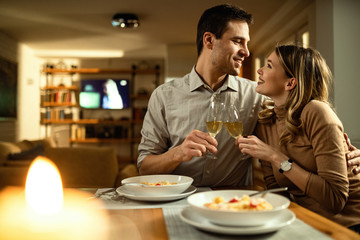 Embraced couple looking at each other while toasting with Champagne at dining table.