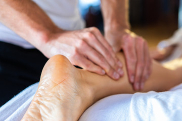 Oil leg massage therapy. Masseur massaging young female legs in a cosy home environment. Body care and skin care concepts