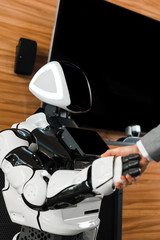 partial view of businessman shaking hands with humanoid robot in office
