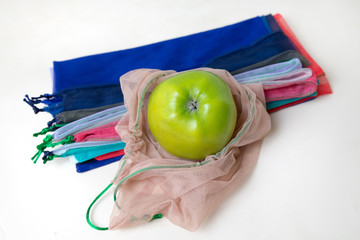 Close up green apple in beige eco bag on the kitchen table on the background of colored bags. Zero waste concept. View from above