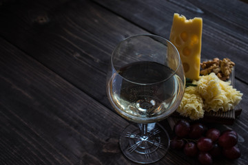 White burgun wine with maasdam cheese, walnut and red grapes on a blackboard on a dark wood background.