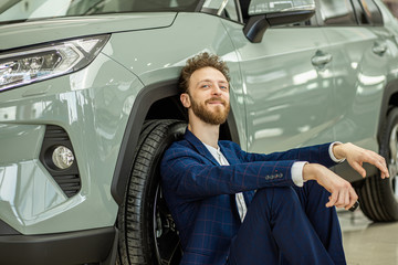 happy young caucasian guy after getting keys from new car, smiling man in formal suit sit on the...
