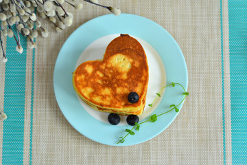 American pancakes on blue plate on white table with spring flowers.Breakfast on Valentine's Day or 8 March - pancakes in the shape of a heart.Pancake week.