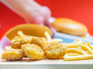 Closeup of crispy nuggets with blurry woman 's hand, fish burger and red background.