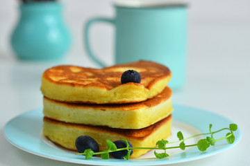 American pancakes on blue plate for healthy breakfast on white table with spring flowers.Breakfast on Valentine's Day or 8 March - pancakes in the shape of a heart.Pancake week.