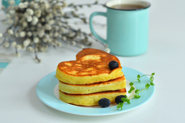 American pancakes on blue plate for healthy breakfast on white table with spring flowers.Breakfast on Valentine's Day or 8 March - pancakes in the shape of a heart.Pancake week.