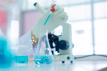 close up scientist using pipette to pouring into flask to blending liquid solution (with chemistry icon) to research and experiment and development about anti-virus pharmaceutical at laboratory center