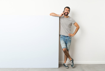 Young handsome man with beard holding a big blue empty placard keeping a conversation with the mobile phone