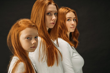 side view on beautiful red haired young girls seriously looking at camera, isolated over black...