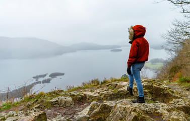 A female hiker in a red jacket standing on top on Surprise viewpoint in Lake District, United Kingdom