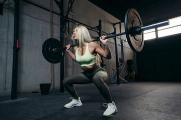 Fototapeta na wymiar Young blonde woman with barbell flexing muscles and making shoulder press squat.