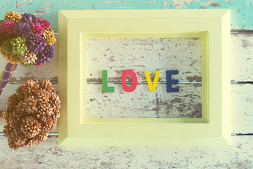 Wooden picture frame placed on a vintage wooden table with two bouquet flowers decorated on the side. The wooden letters placed in the picture frame signify love.Valentine Day Concept