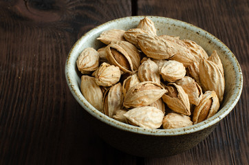 Almonds in nutshell in cup on wooden background