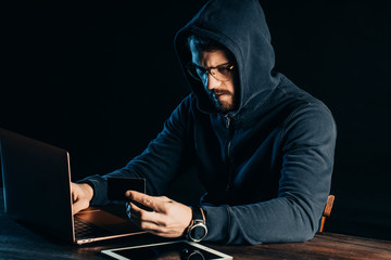 young caucasian man hacking bank card using computer system, male wearing pullover, sit in the hood...