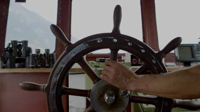 The captain turns the wooden wheel on the old ship