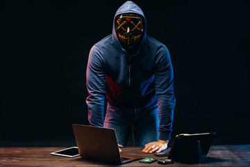 anonymous masked hacker man over dark space, terrifying male sit with laptop, want to get access to data. young hacker have his own methods to access to any kind of system wherever