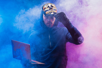 hacker male use laptop to gain unauthorized access to data, in dark smoky space with neon lights....