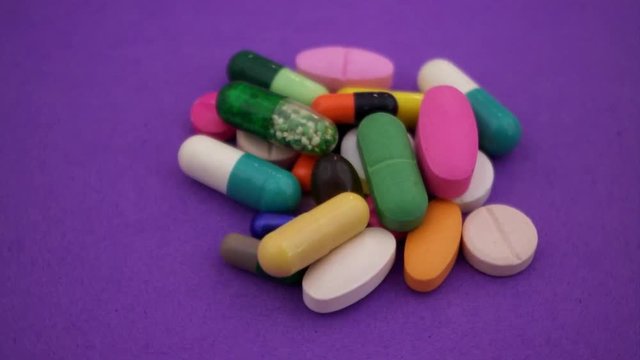Heap of colorful pills and drugs on purple background