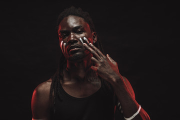portrait of serious black african man smearing white strips on the face, young muscular gangster male with dreadlocks confidently look at camera. studio shot