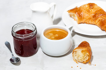 cup of espresso and fresh croissants, berry jam for breakfast on white table, top view