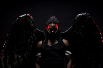 portrait of strong dark angel isolated over black background, young african man with dreadlocks became an angel after death. angel with strong muscles and fit body came down from heaven. studio shot