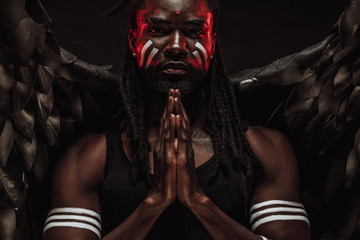 portrait of black african angel praying isolated over black background and looking at camera....