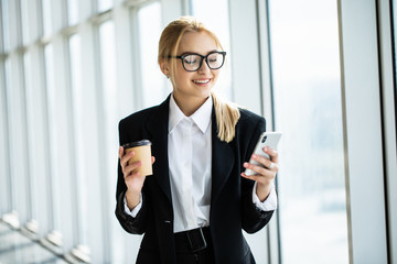 Businesswoman taking a coffee break and using smartphone in office