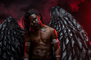 strong muscular angel with black wings fall on the earth, extraordinary african man stand in the flesh of dark angel and illustrated dark forces. isolated photoshoot