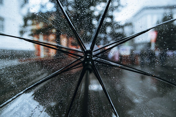 Open transparent umbrella with the raindrops on it. Rainy weather in the streets of a busy city....
