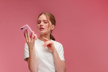 Confused young redhead woman holding pink smartphone.Embarassed girl has problem with broken not...