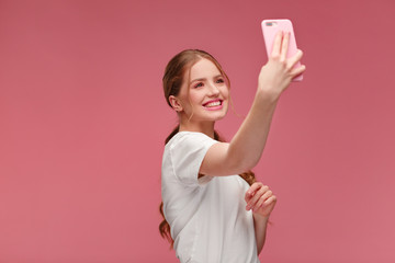 Funny young redhead woman making selfie. Smiling girl wearing white t-shirt holding pink...