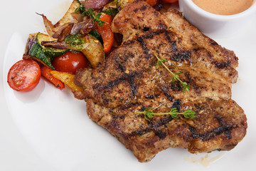 Grilled pork steak with sauce and vegetable on white plate