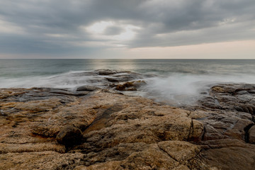Waves breaks rocky ocean coast under dramatic sky with clouds on Sri Lanka island.