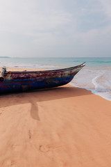 Obraz premium Traditional fisherman's boat on the sand of Sri Lanka island beach on a ocean coast in front of turquoise ocean waves.