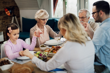 Multi-generating family saying grace while holding hands at dining table.